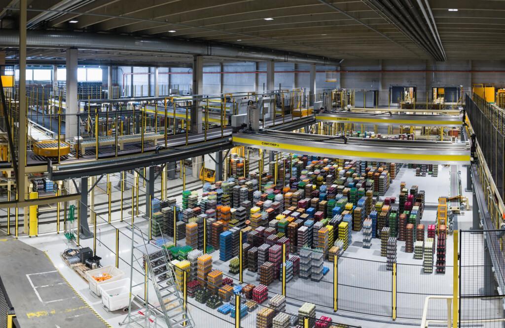 Cimcorp overhead gantry robot managing diverse beverage SKUs — bottles of varying products and packaging — in an automated warehouse setting.